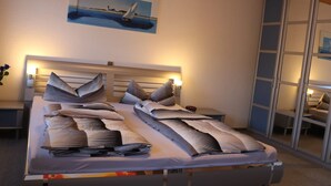 A neatly made bed with striped bedding, a headboard with integrated lighting, a painting of a sailboat on the wall, and a sliding glass door leading to a balcony.