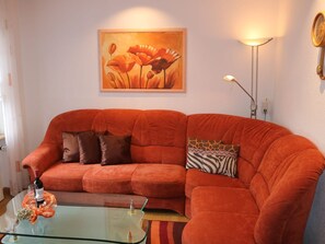 Een woonkamer met een rode bank, een glazen salontafel en een schilderij aan de muur.