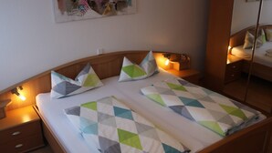 A double bed with geometric-patterned bedding, bedside lamps, a nightstand, and a wall-mounted artwork. - Apartment '45qm' with Mountain View, Shared Garden and Wi-Fi (Schonach im Schwarzwald)