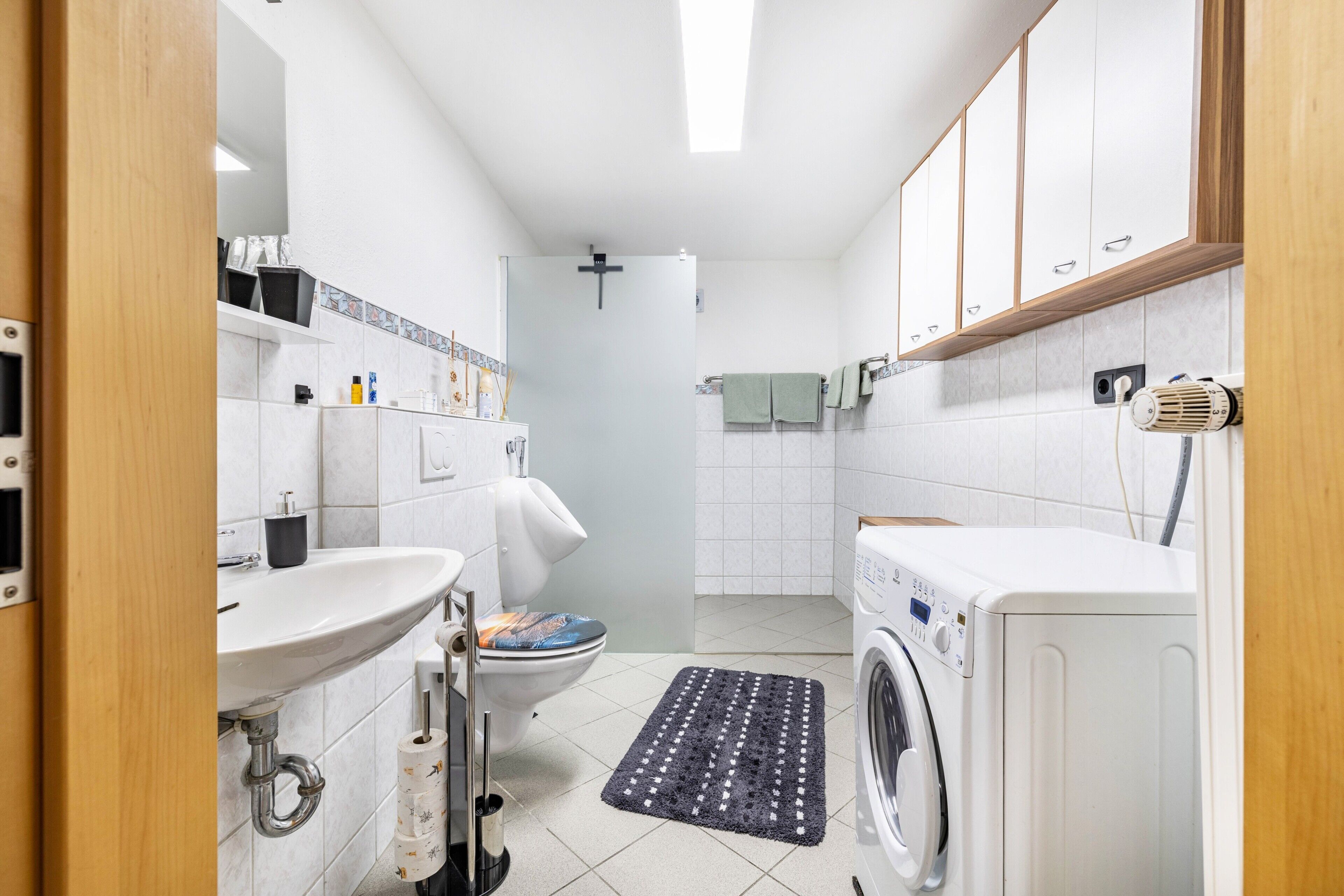 A modern bathroom with a sink, toilet, shower, and washing machine.