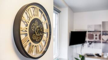 Een wandklok met Romeinse cijfers en tandwielen, een raam, en een bureau met een computer monitor.