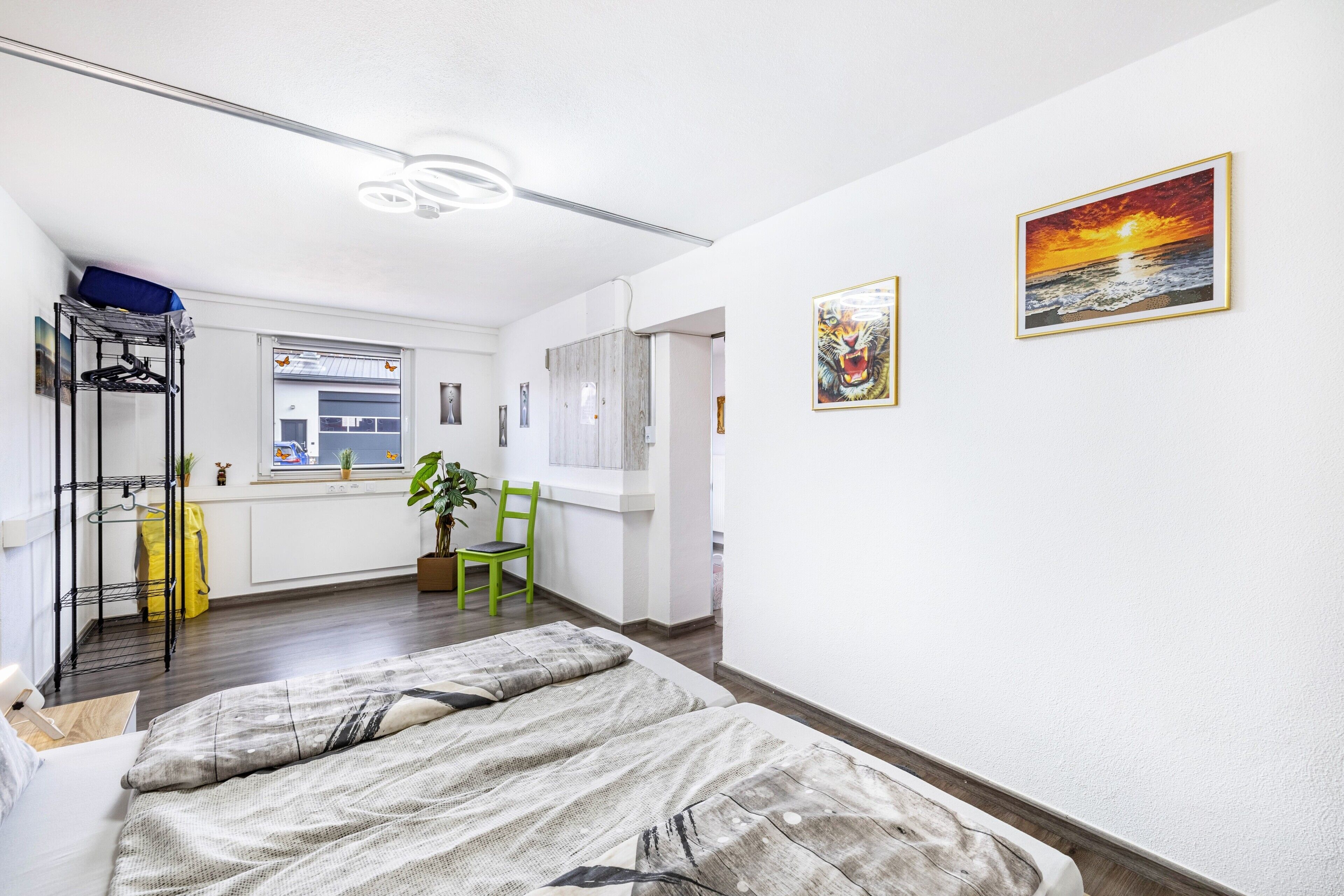 Een slaapkamer met een bed, een stoel, een raam, een plant en een schilderij aan de muur.