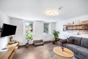 Ein modernes Wohnzimmer mit Fernseher, einer Couch, einem Couchtisch und einem großen Fenster.