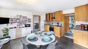 Une cuisine moderne avec des meubles en bois, un coin repas doté d’une table ronde et un téléviseur fixé au mur.