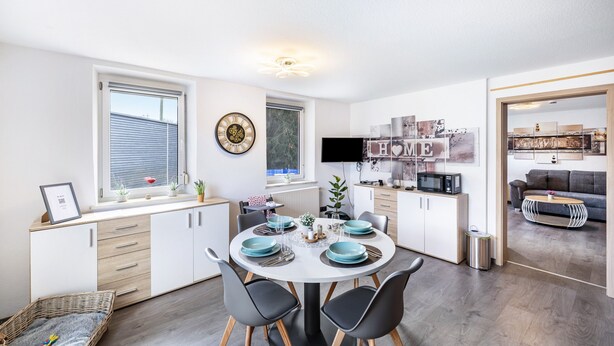 Une cuisine moderne avec un coin repas, des meubles blancs et un téléviseur à écran plat.