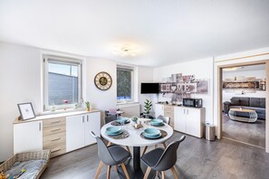 A modern kitchen with a dining area, white cabinetry, and a flat-screen TV. - Leas Apartment with Wi-Fi (Aichen)