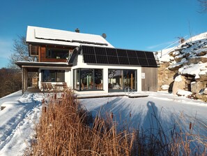 A modern two-story house with a solar panel roof, large glass windows, and a stone wall. - Holiday Home 'Am Teich' with Mountain View, Private Terrace and Wi-Fi (Sankt Leonhard bei Freistadt)