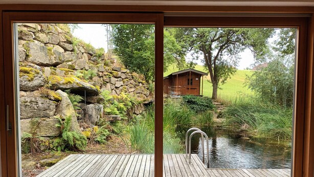 A wooden deck with a stone wall and a small pond. - Holiday Home 'Am Teich' with Mountain View, Private Terrace and Wi-Fi (Sankt Leonhard bei Freistadt)