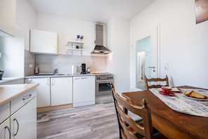Eine kleine Küche mit weißen Schränken, einem eingebauten Ofen und einem Essbereich mit Holztisch und -stühlen.
