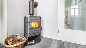 Una habitación moderna con un hogar a leña, una cesta de mimbre con leña y un ventanal que da a otra zona.