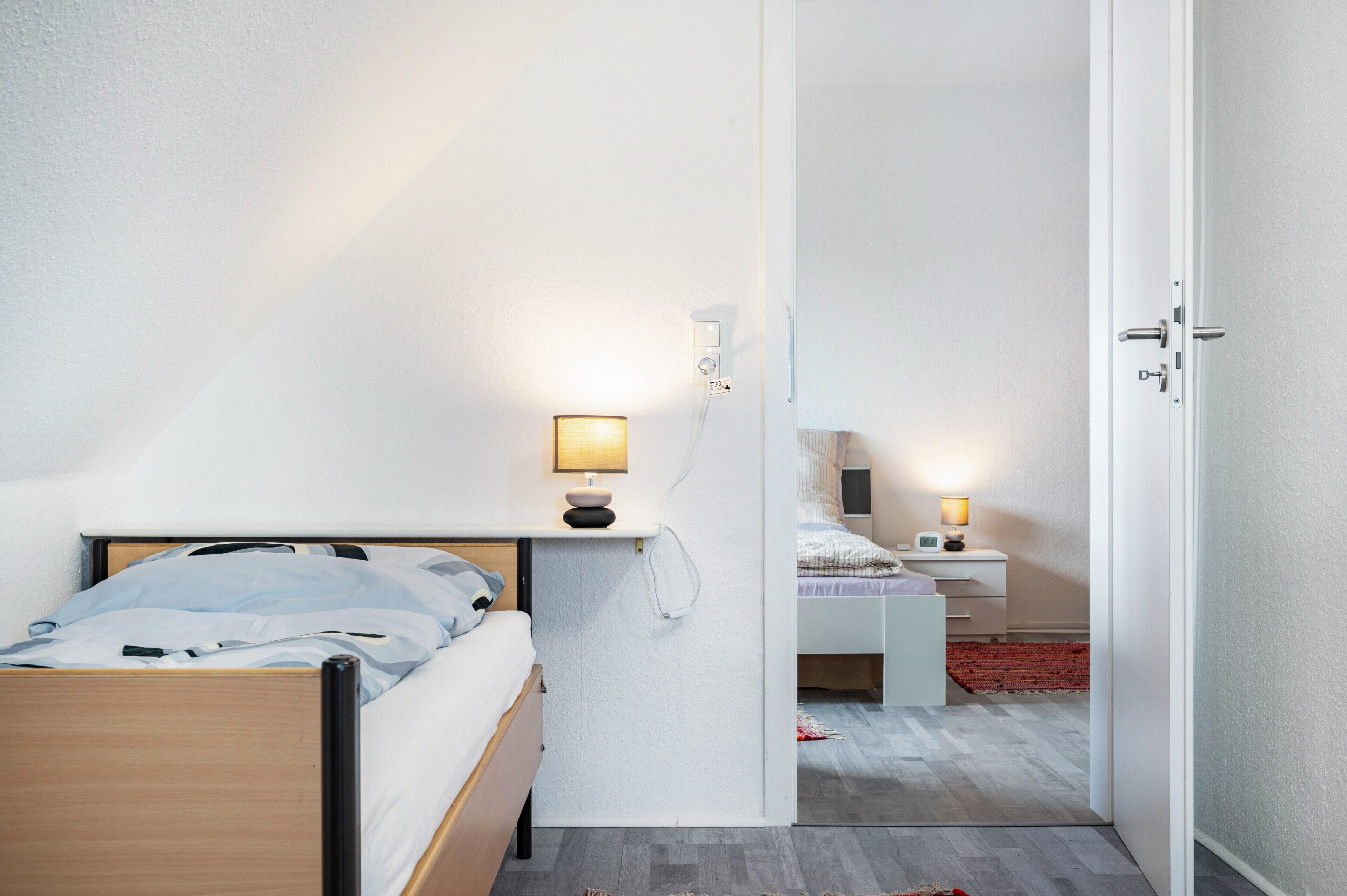 Une chambre à coucher comprenant un lit, une table de chevet, une lampe et une porte donnant sur une autre pièce.