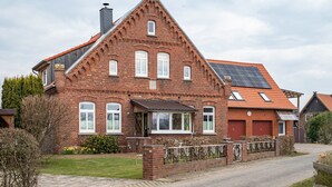 Una casa de ladrillo rojo con techo inclinado, paneles solares y un patio cercado.
