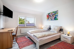 Ein Schlafzimmer mit Bett, Nachttisch, Fernseher, Fenster und Kunstwerk.