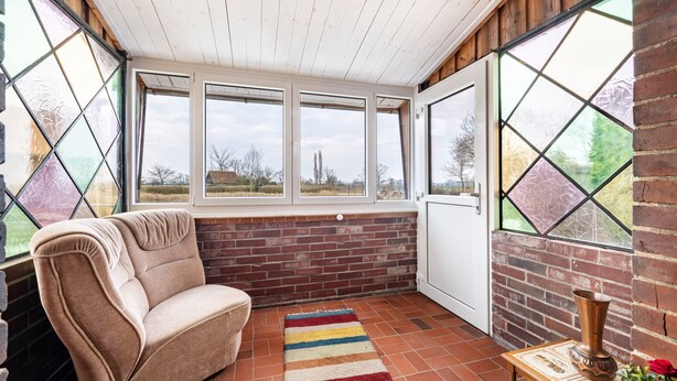 Una habitación acogedora con pared de ladrillo, un banco acolchado, una alfombra colorida y una ventana con vistas a árboles.