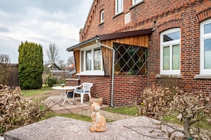 Ein Backsteinhaus mit Terrasse, einem weißen Stuhl und einer Katzenfigur.