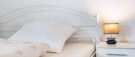 A bed with a white headboard, a bedside table with a lamp, and a white drawer.