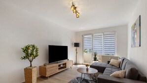 A modern living room with a flat-screen TV, a sofa, a coffee table, and a potted plant.