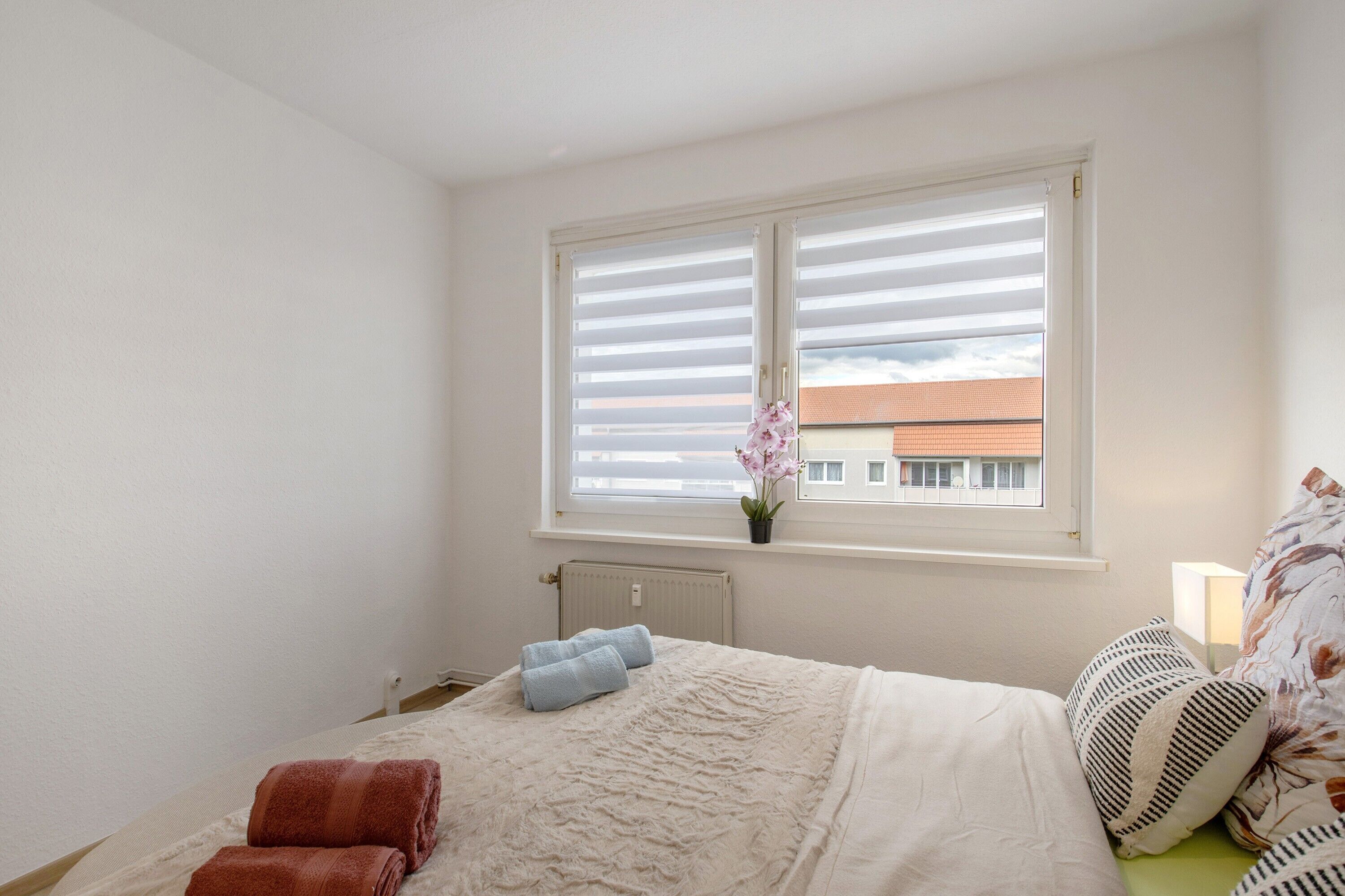 Un dormitorio con cama, ventana con persianas, radiador y una planta en maceta.