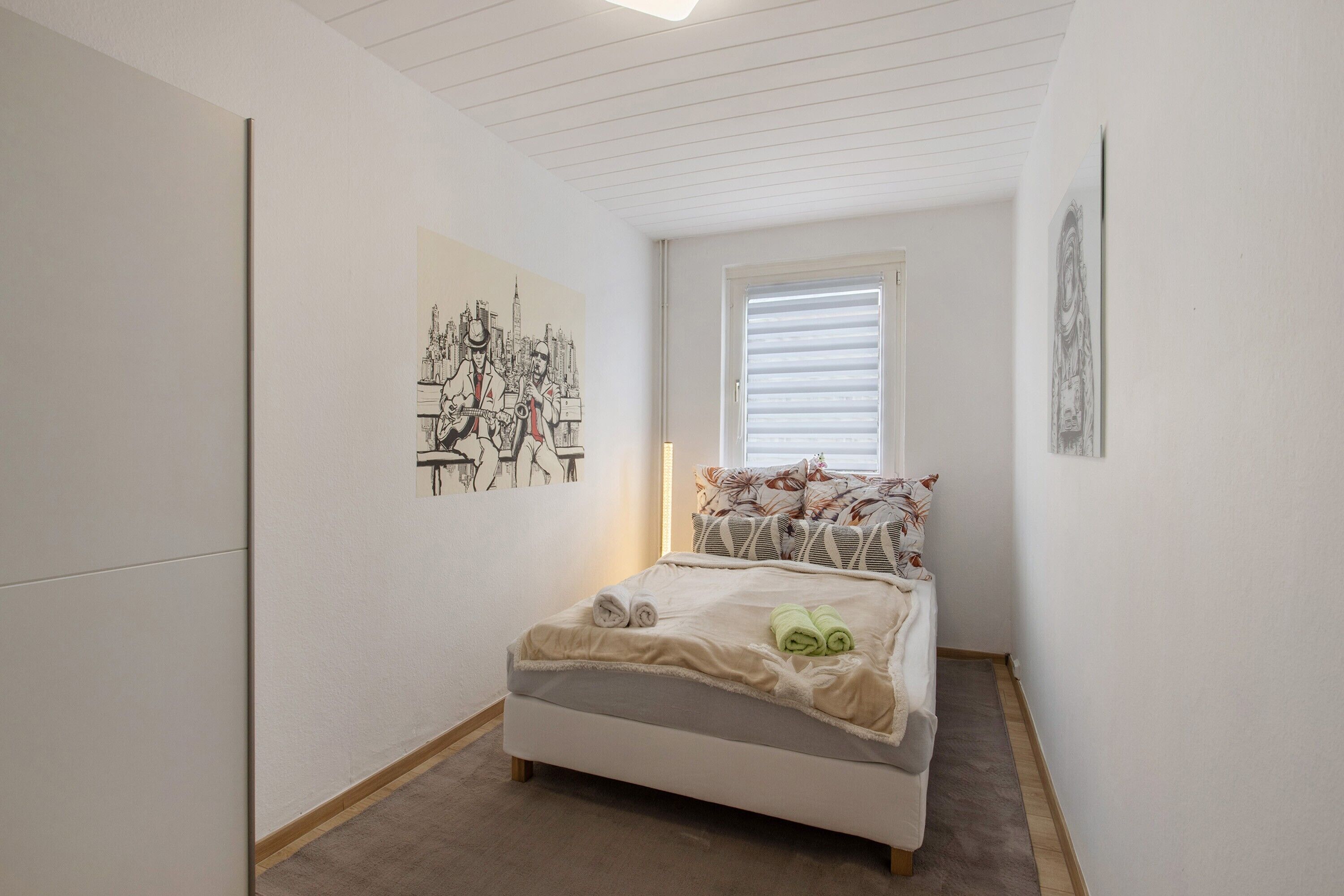 A bedroom with a bed, a window with blinds, and artwork on the walls.