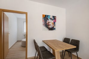 Un comedor con una mesa de madera y cuatro sillas, un cuadro en la pared y una puerta que da a otra habitación.