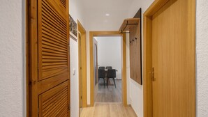 A hallway with wooden doors, a dining area with a table and chairs, and a white wall.
