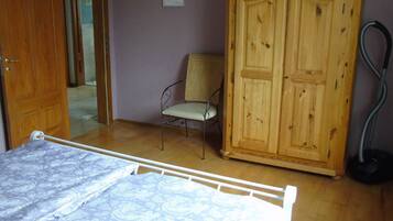 A bedroom with a bed, a wooden wardrobe, a chair, and a vacuum cleaner.