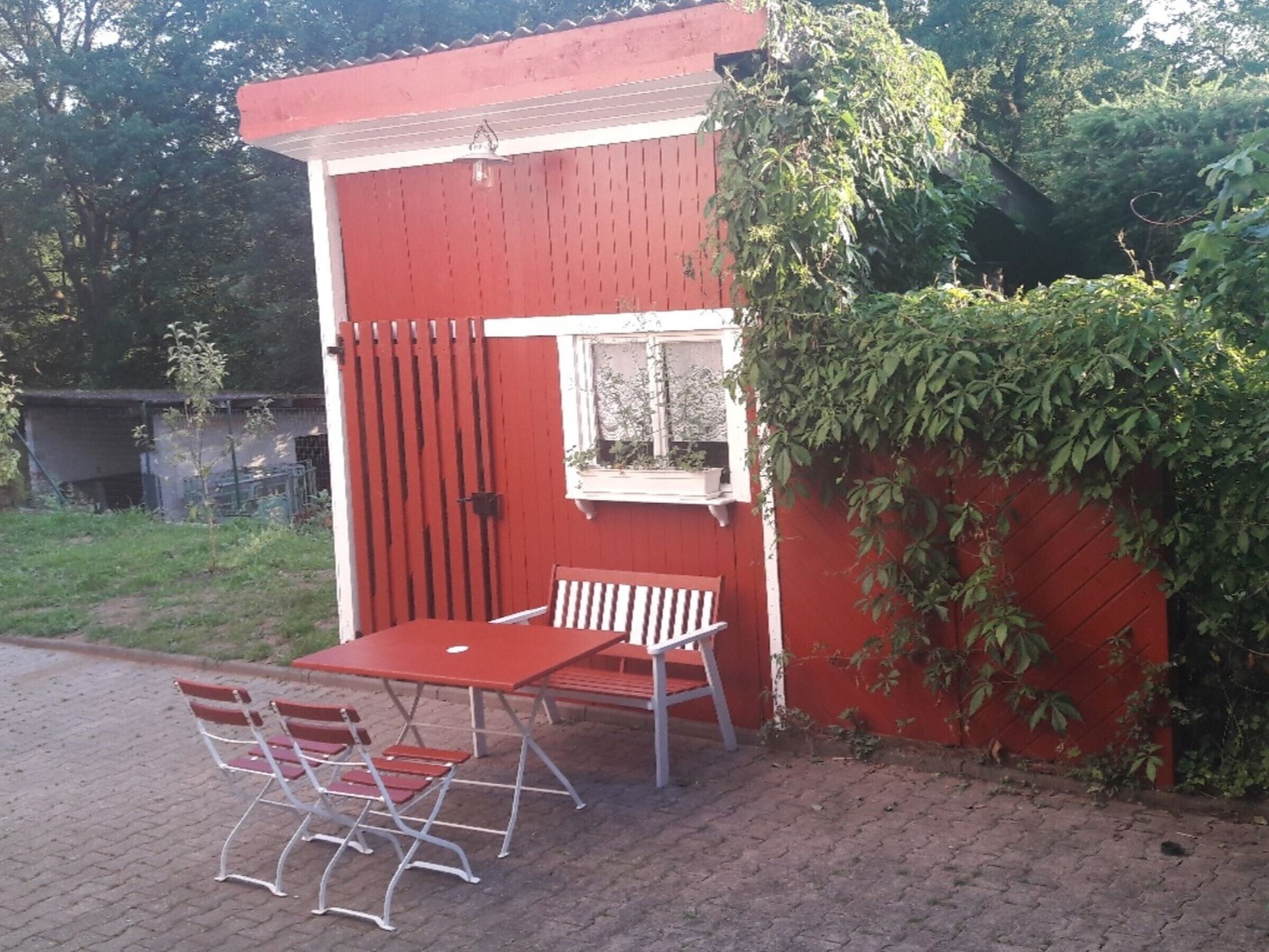 Un bâtiment rouge avec une fenêtre, une porte et une petite table entourée de chaises à l’extérieur.
