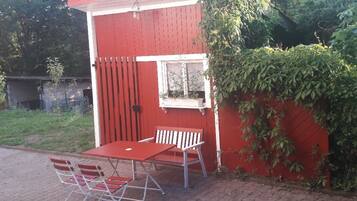 Un bâtiment rouge avec une fenêtre, une porte et une petite table entourée de chaises à l’extérieur.