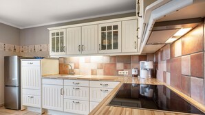 Une cuisine avec des meubles blancs, un réfrigérateur en acier inoxydable, une plaque de cuisson à induction noire et un dosseret carrelé.