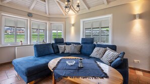 Un salon chaleureux avec un canapé d’angle bleu, une table basse en bois et une vue sur l’extérieur grâce à de grandes fenêtres.