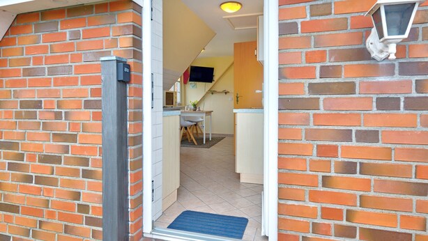 Een gevel van baksteen met een deur, een blauwe mat bij de ingang en een wandlamp.