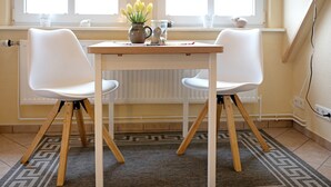 Een kamer met een tafel, twee stoelen, een raam met uitzicht, een radiator en een kamerkleed met patroon.