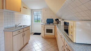 Een keuken met een spoelbak, fornuis, magnetron en kastjes.