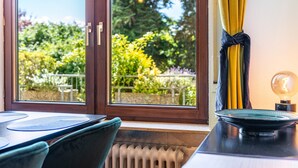 A room with a view of greenery outside, a radiator, a table with a placemat, and a lamp on a table.