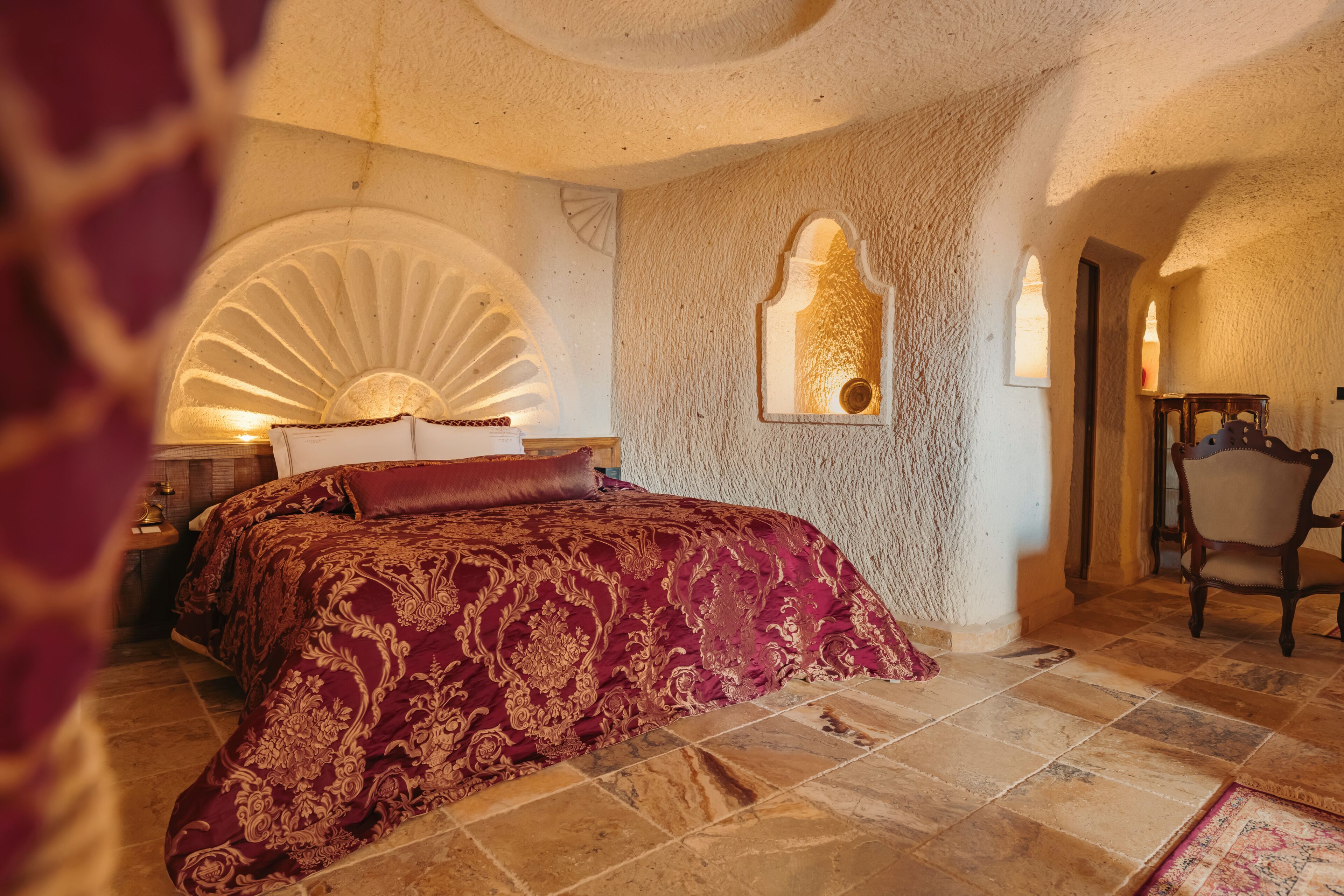 Een kamer met een groot bed, een nachtkastje, een stoel en een muur met een decoratieve boog.