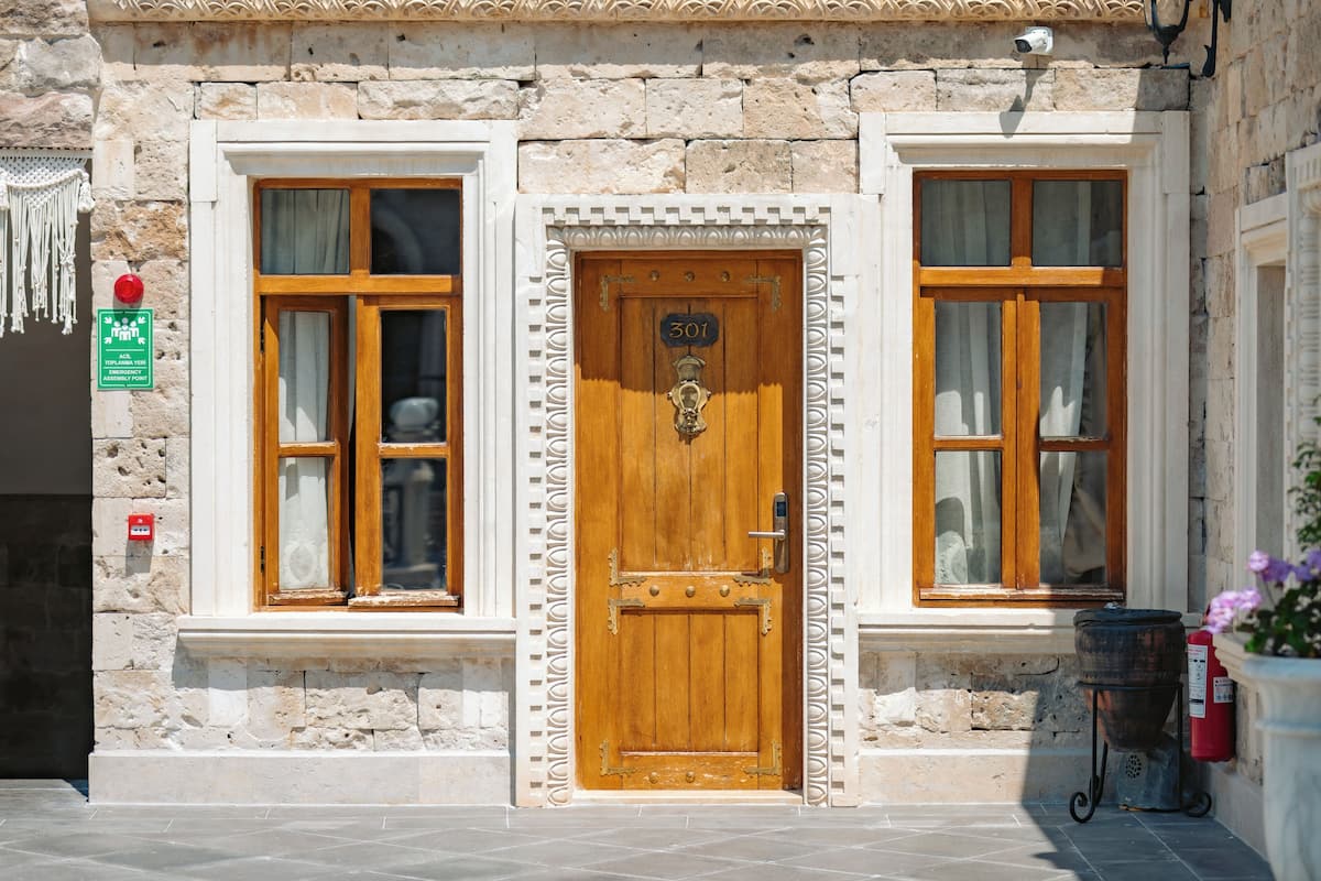 A stone building with a wooden door marked '301,' two windows with curtains, a fire extinguisher, and a sign indicating a top floor emergency exit.