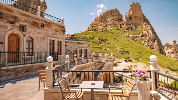 Una terraza con paredes de piedra, muebles de madera y vistas a colinas rocosas.