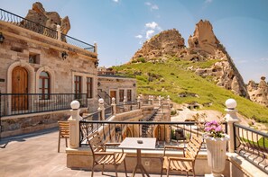 A terrace with stone walls, wooden furniture, and a view of rocky hills.