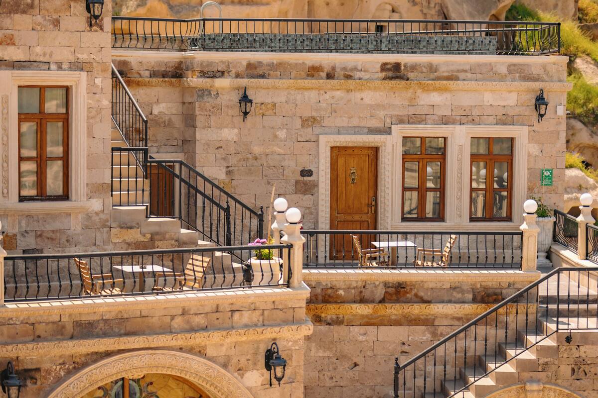 Un edificio de varios pisos con paredes de piedra, balcones con barandillas y zonas de estar al aire libre.