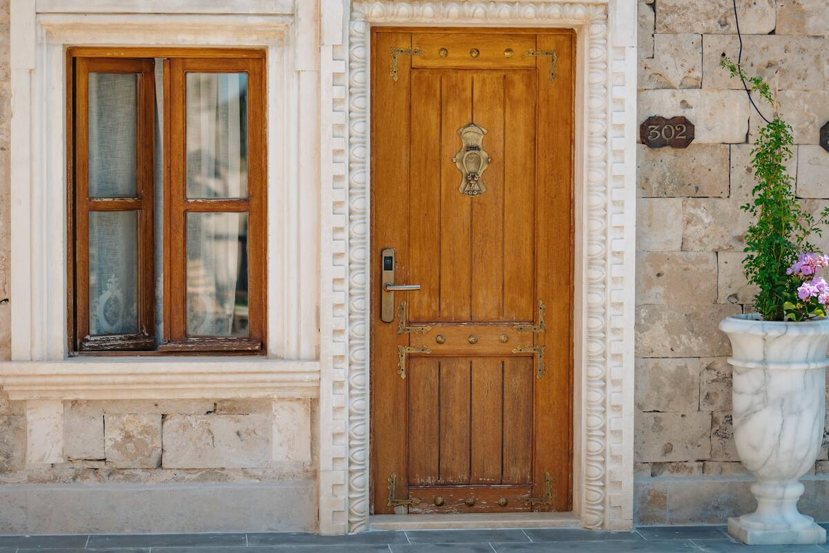 Una puerta de madera con un aldabón de latón, una ventana con marco de madera y un muro de piedra con placa de número.