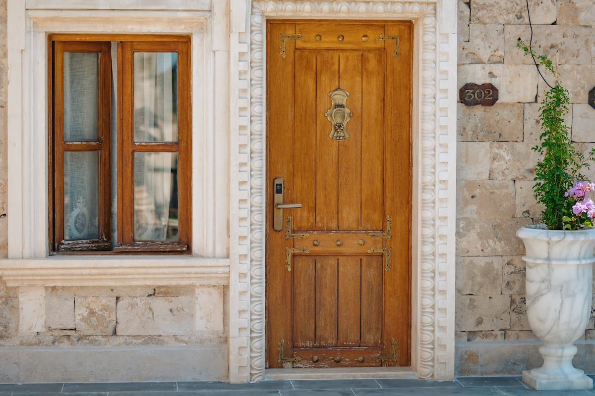 A wooden door with a brass knocker, a window with a wooden frame, and a stone wall with a number plaque.