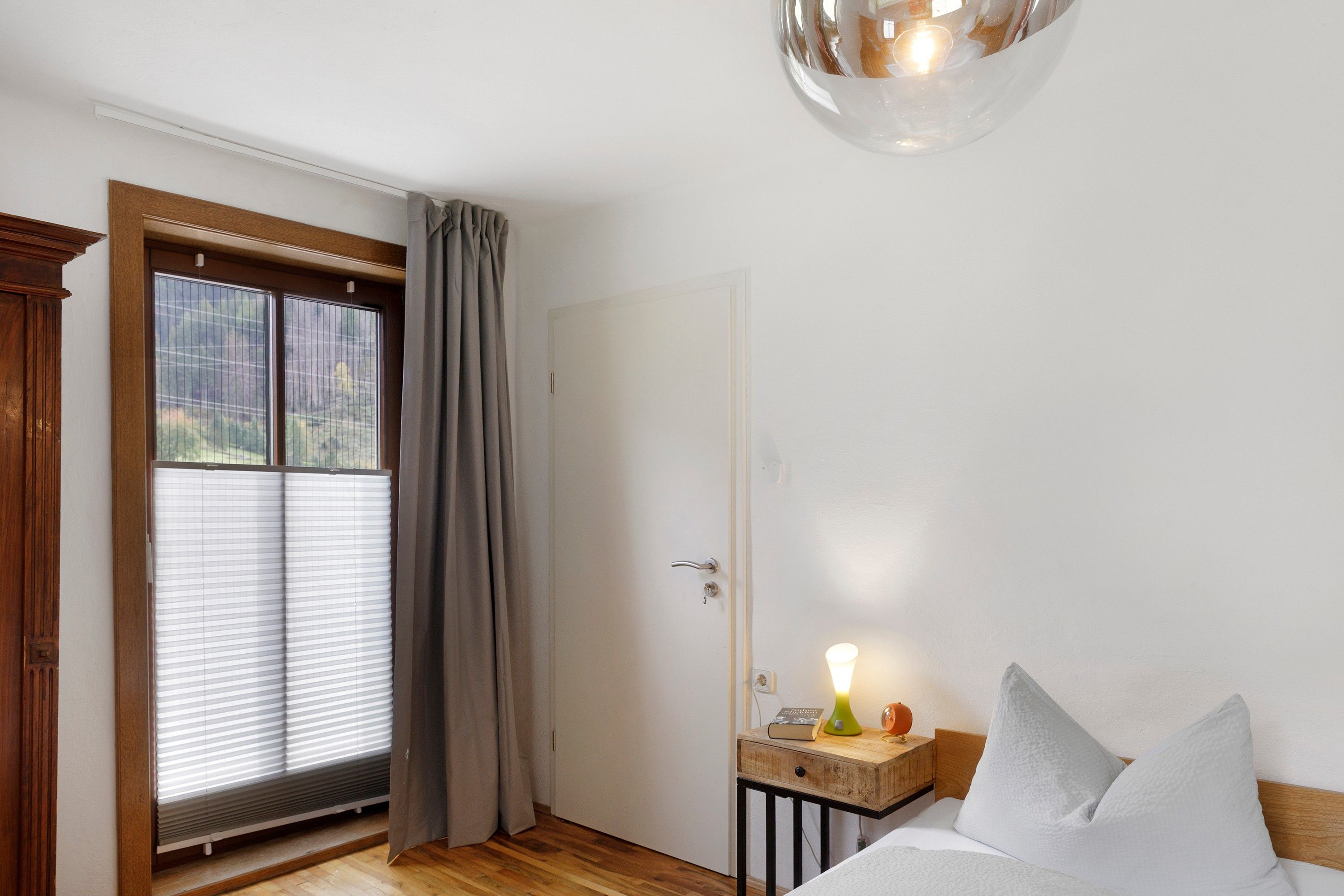 Ein Schlafzimmer mit einem hölzernen Bett, einem Nachttisch mit Lampe und einem Fenster mit Jalousien.
