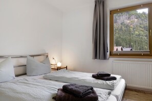 A bedroom with two beds, a nightstand, a lamp, a window with a view of trees, and a radiator.