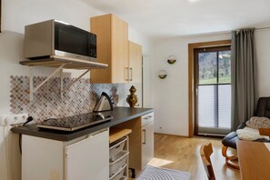 A compact kitchen with a microwave, a kettle, and a sink. There is a dining area with a table and chairs, and a window with curtains. - Apartment 'Mizi' with Mountain View, Balcony and Wi-Fi (Stall)