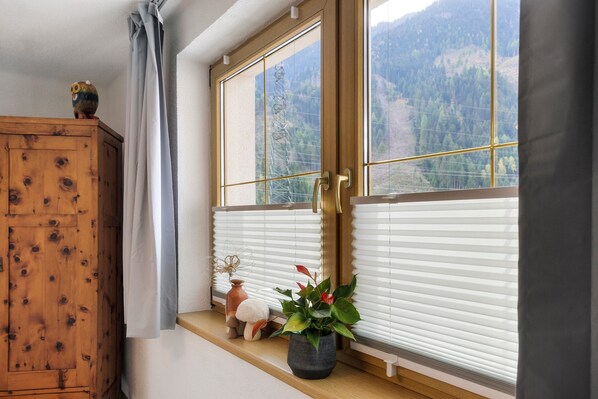 A room with a wooden cabinet, a window with blinds, and a shelf with decorative items.