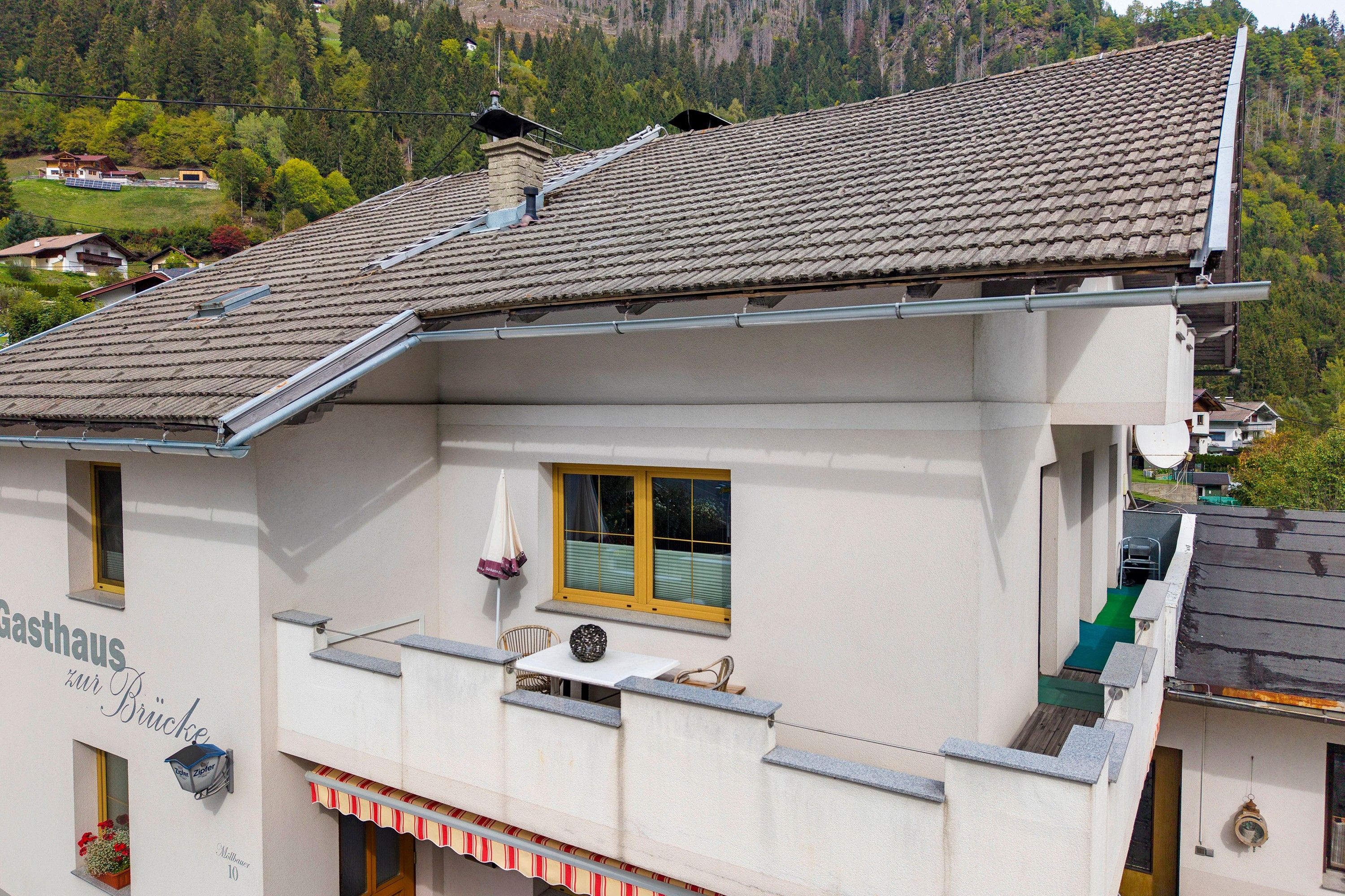 A building with a tiled roof, a balcony with a railing, and a window with a view of the surrounding landscape.
