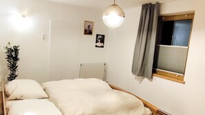 Ett sovrum med en säng i trä, ett nattduksbord med en lampa, ett fönster med gardiner och en tavla som hänger på väggen.