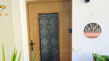 Uma porta de madeira com um painel de vidro decorativo, uma cadeira de metal com almofada verde, uma planta em vaso e um aplique de parede.