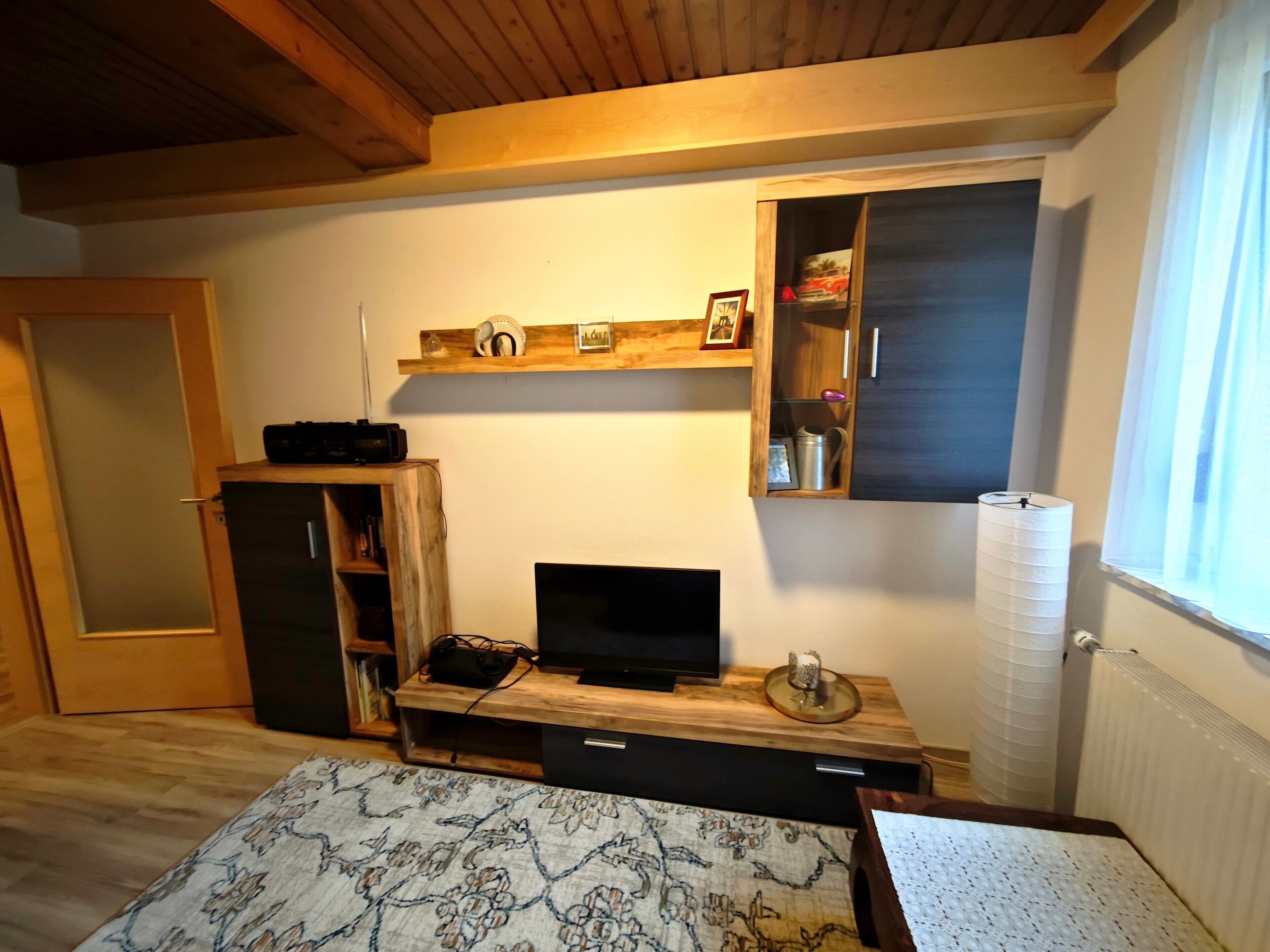 A room with a wooden desk, a television, a bookshelf, and a window with curtains.