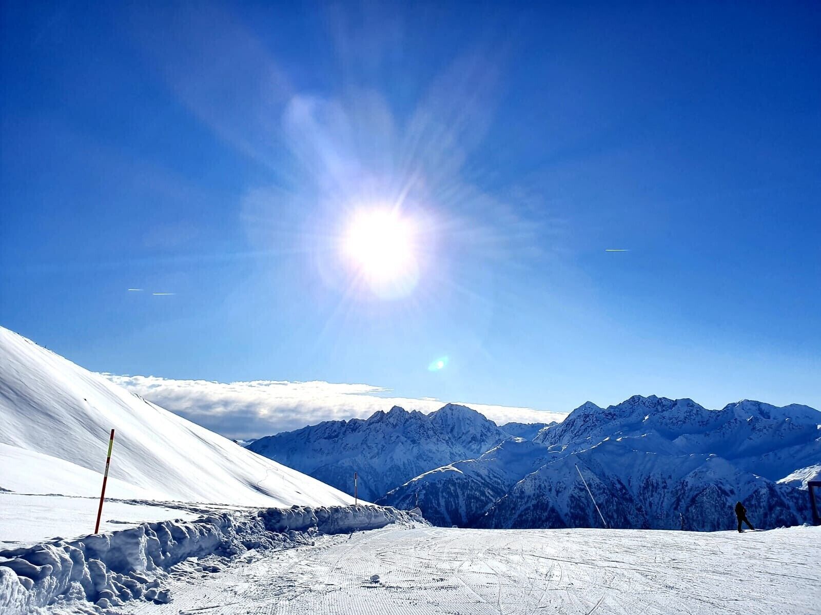 Paisaje montañoso nevado con cielo despejado y sol brillante.